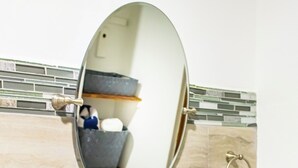 A bathroom with a white sink, a round mirror, and a glass shelf.
