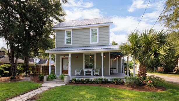 A two-story house with a porch, a small garden, and a pathway leading to the entrance.