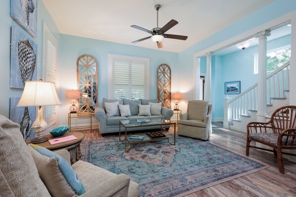 A living room with a blue wall, a ceiling fan, a sofa, a coffee table, and a patterned rug.