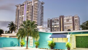 Un moderno edificio residencial de varios pisos con balcones, una pared verde y plantas en macetas.