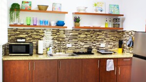 Una cocina con armarios de madera, encimera de granito, microondas, lavabo y diversos utensilios de cocina en estantes.
