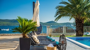 A poolside area with lounge chairs, a small pool, and a view of the sea and hills.