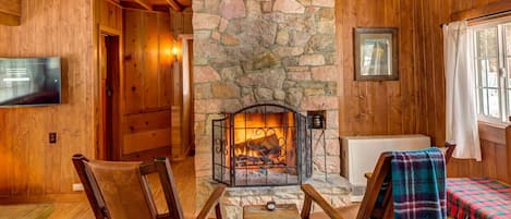 A cozy cabin interior with a stone fireplace, wooden walls, and a television mounted on the wall.