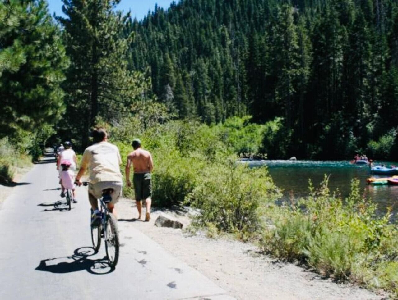 Un chemin pavé longe une rivière, avec des cyclistes et un bateau en arrière-plan.