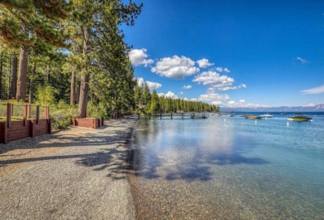 A clear lake with a wooden walkway and trees on one side, and boats on the water.