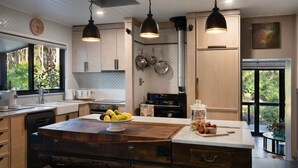 Cocina moderna con armarios de madera, una isla central con frutas, ollas colgantes e iluminación colgante.