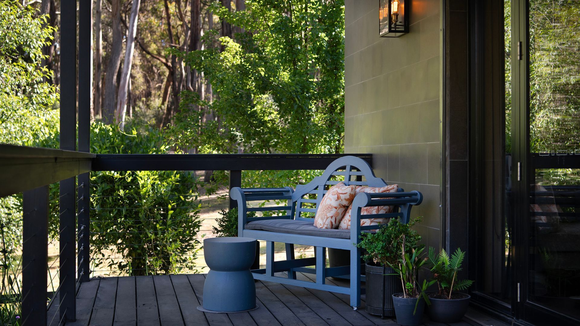 A wooden deck with a blue bench and potted plants, overlooking a lush garden.