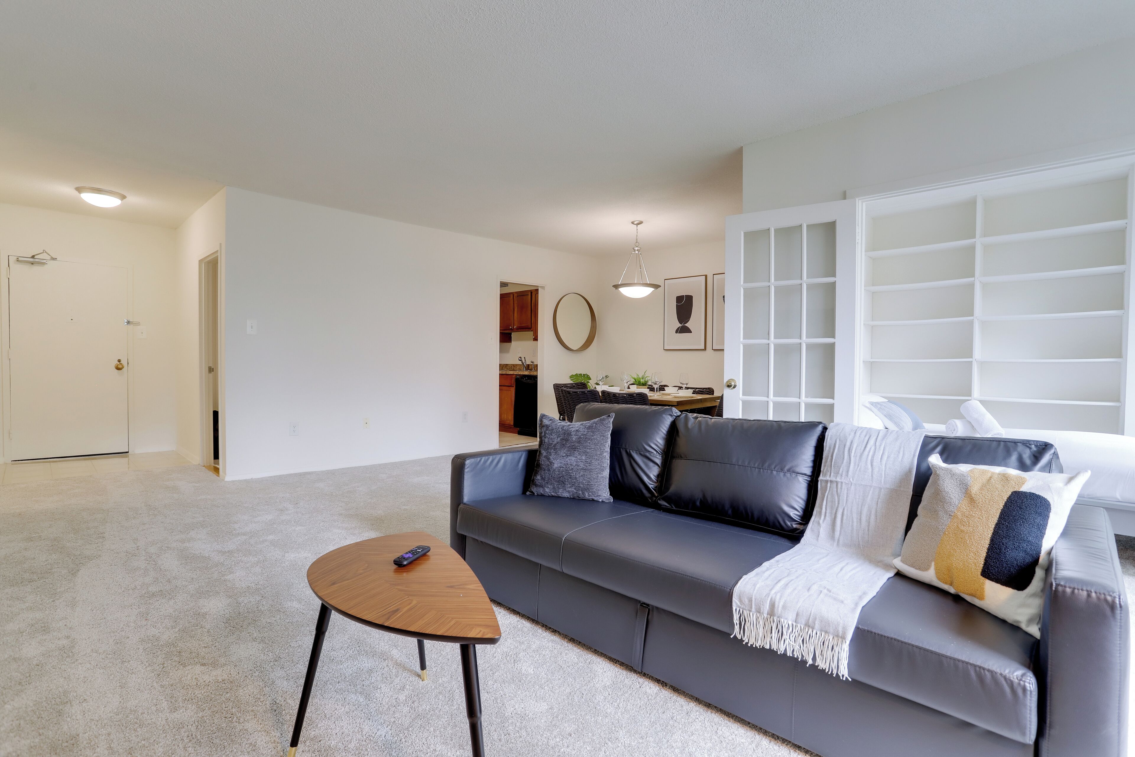 A living room with a grey sofa, a coffee table, and a dining area in the background.