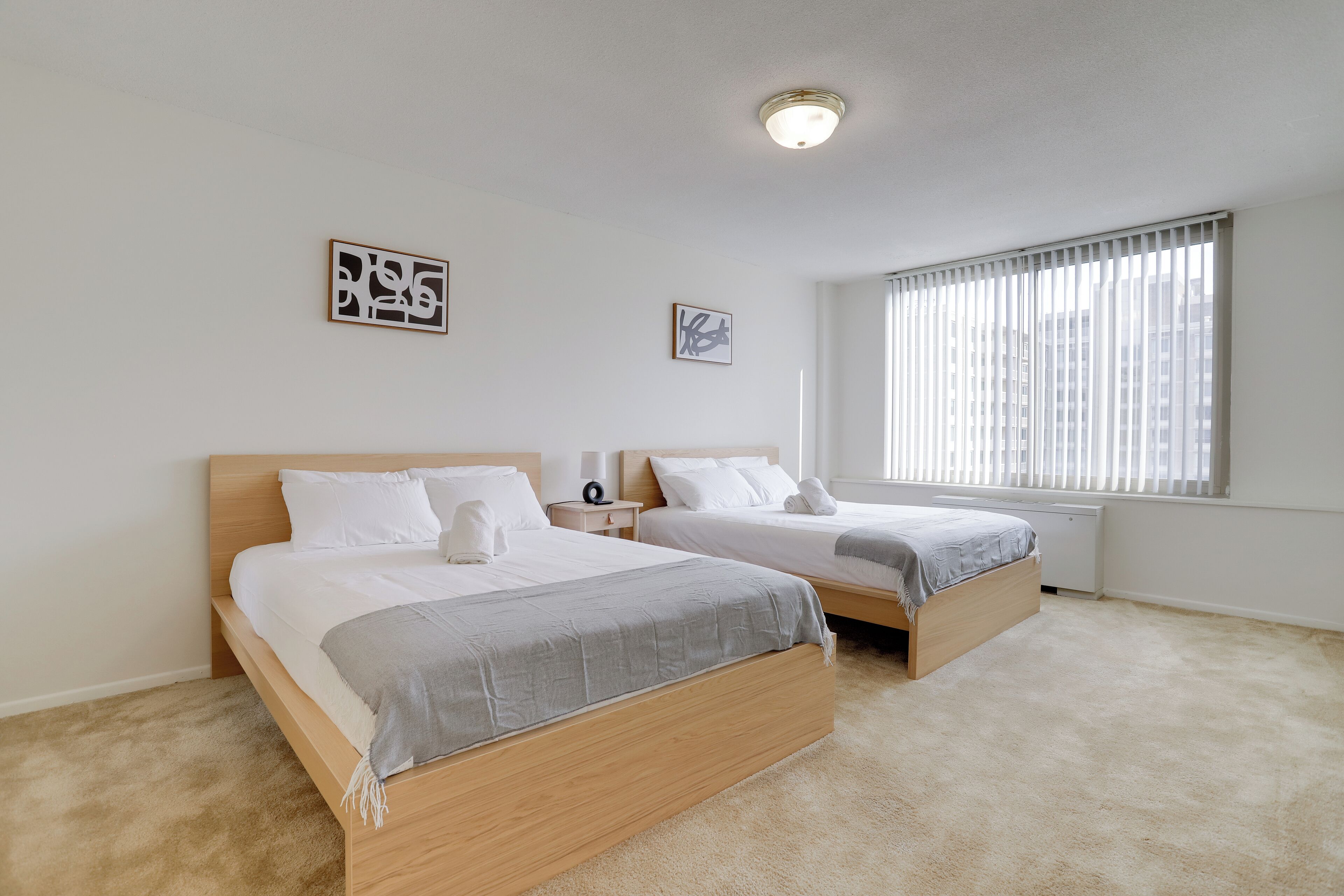 A bedroom with two beds, a window with blinds, and a ceiling light.