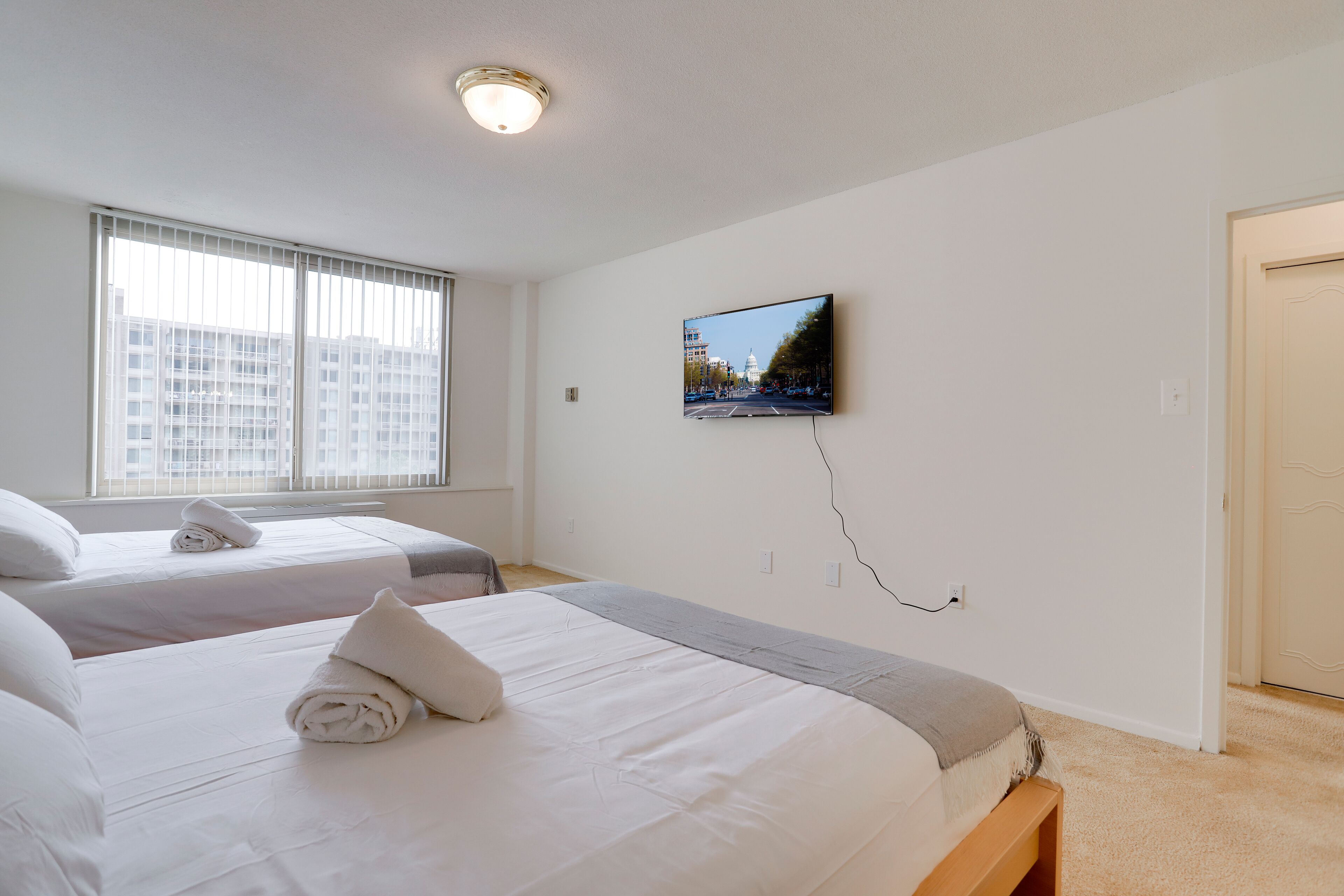 Habitación de hotel con dos camas, un televisor montado en la pared y una ventana con persianas.