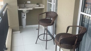 Een balkon met twee rieten stoelen, een klein spoelgedeelte en een raam.