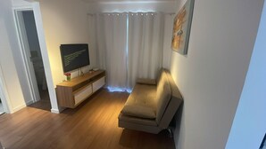 Een woonkamer met een bank, een televisie op een dressoir en een raam met gordijnen.