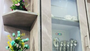 Een keuken met een marmeren aanrecht, een witte pot met bloemen en een glazen kast met keukengerei.