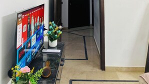 Een moderne woonkamer met een flatscreentelevisie op een zwart voetstuk, een kleine potplant en een decoratief object op de vloer.