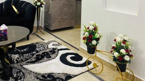Een moderne woonkamer met een zwarte bank, een salontafel, een kamerkleed en een eethoek met een kast en een schilderij.