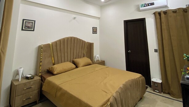 Une chambre à coucher comprenant un lit, une table de chevet, un ventilateur de plafond, un appareil de climatisation et une porte.