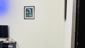 Un salon avec un téléviseur à écran plat fixé au mur, une petite table sur laquelle est posé un vase, et un tableau encadré au-dessus du téléviseur.