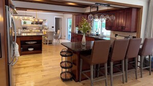 Une cuisine moderne avec des meubles en bois, un îlot central doté de tabourets de bar et un coin repas agrémenté d’un lustre.