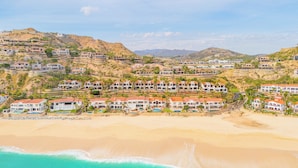 Uma área residencial costeira com casas numa encosta, uma praia e céu claro.