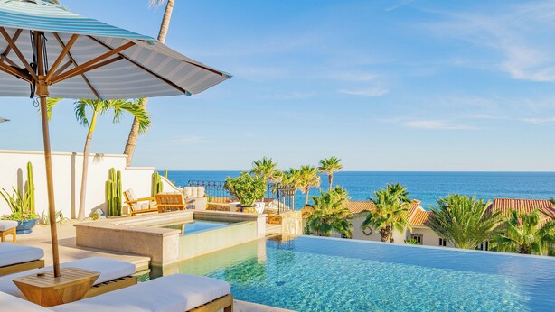 Piscina infinita com espreguiçadeiras e guarda-sóis, com vista para o oceano.