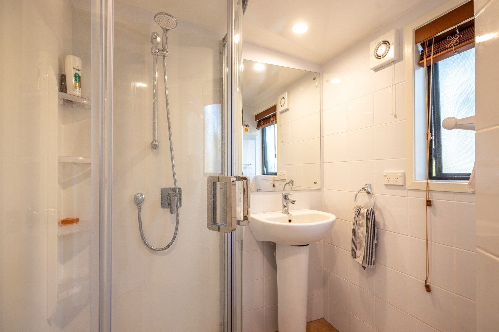 Une salle de bain moderne avec une douche à parois de verre, un lavabo blanc et une fenêtre offrant une belle vue.
