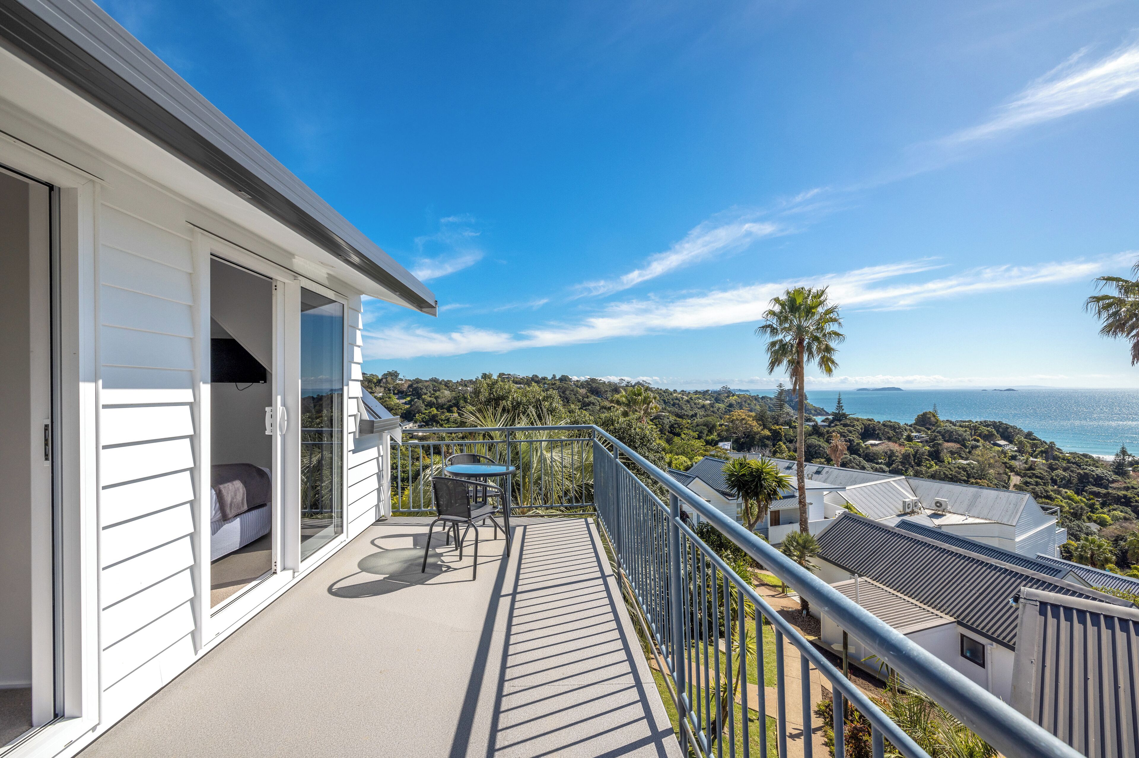 A balcony with a table and chairs, a sliding glass door, and a view of the ocean and hills.