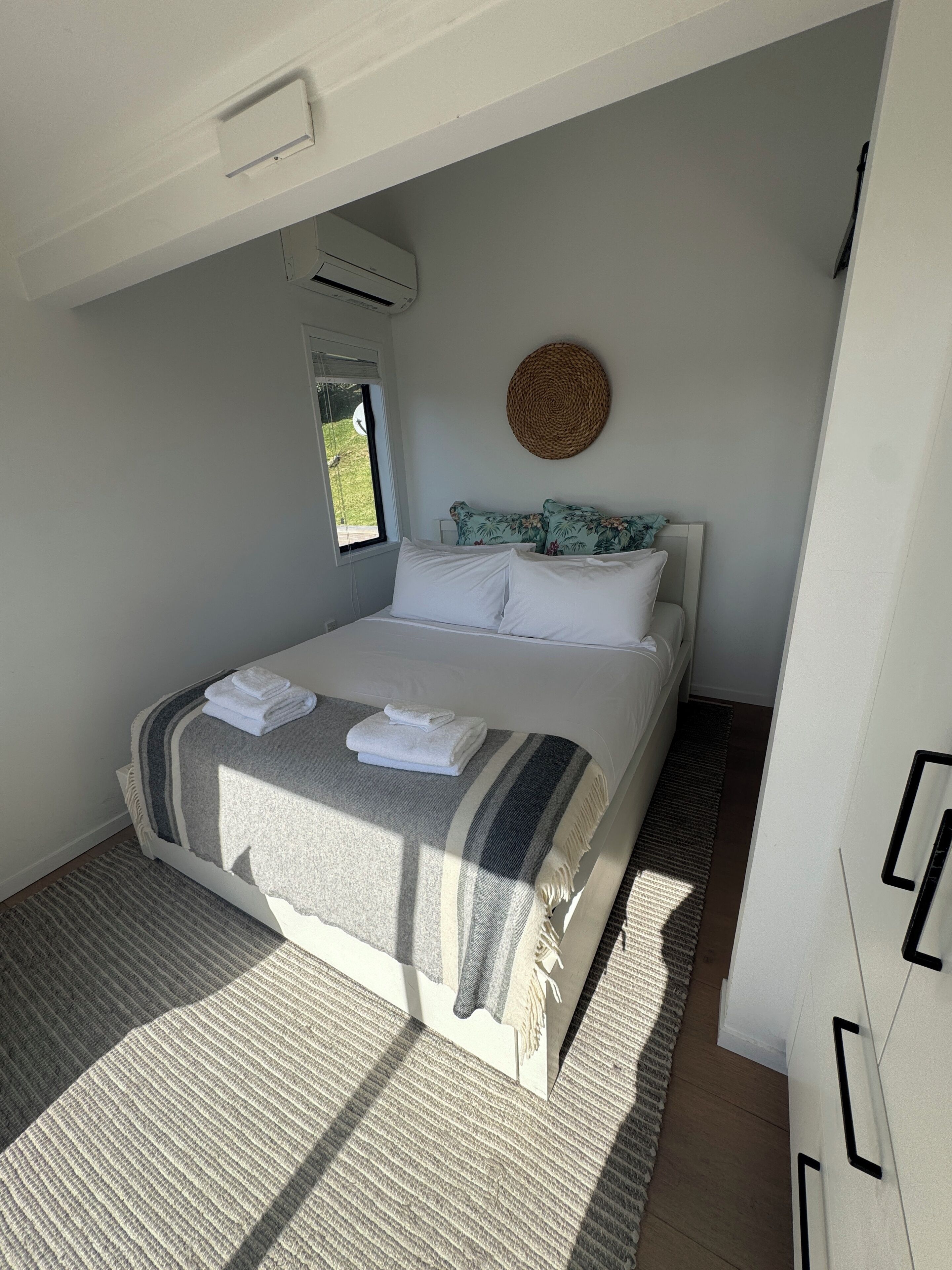Una camera da letto con un letto, una finestra, un condizionatore d'aria, un arazzo e una porta.