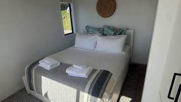 A bedroom with a bed, a window, an air conditioning unit, a woven wall hanging, and a door.