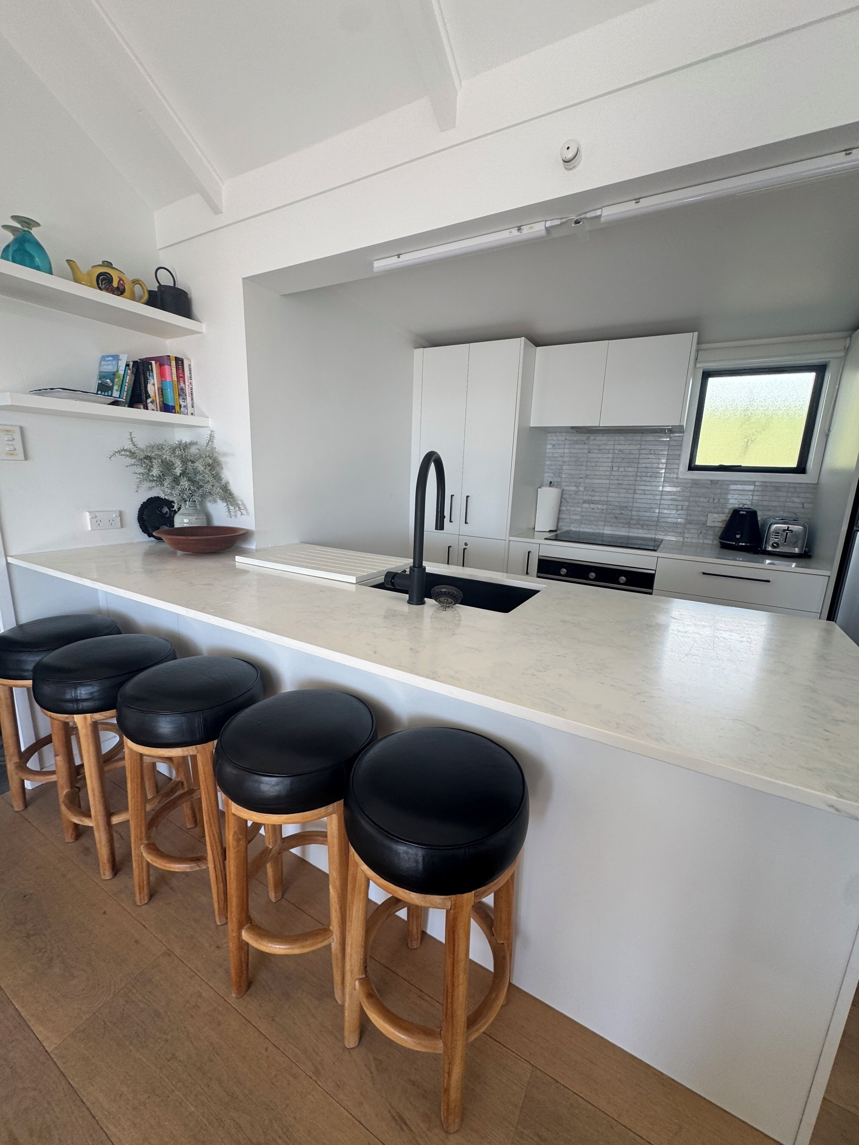 Una cocina moderna con una isla central, taburetes de bar, armarios blancos y un ventanal.