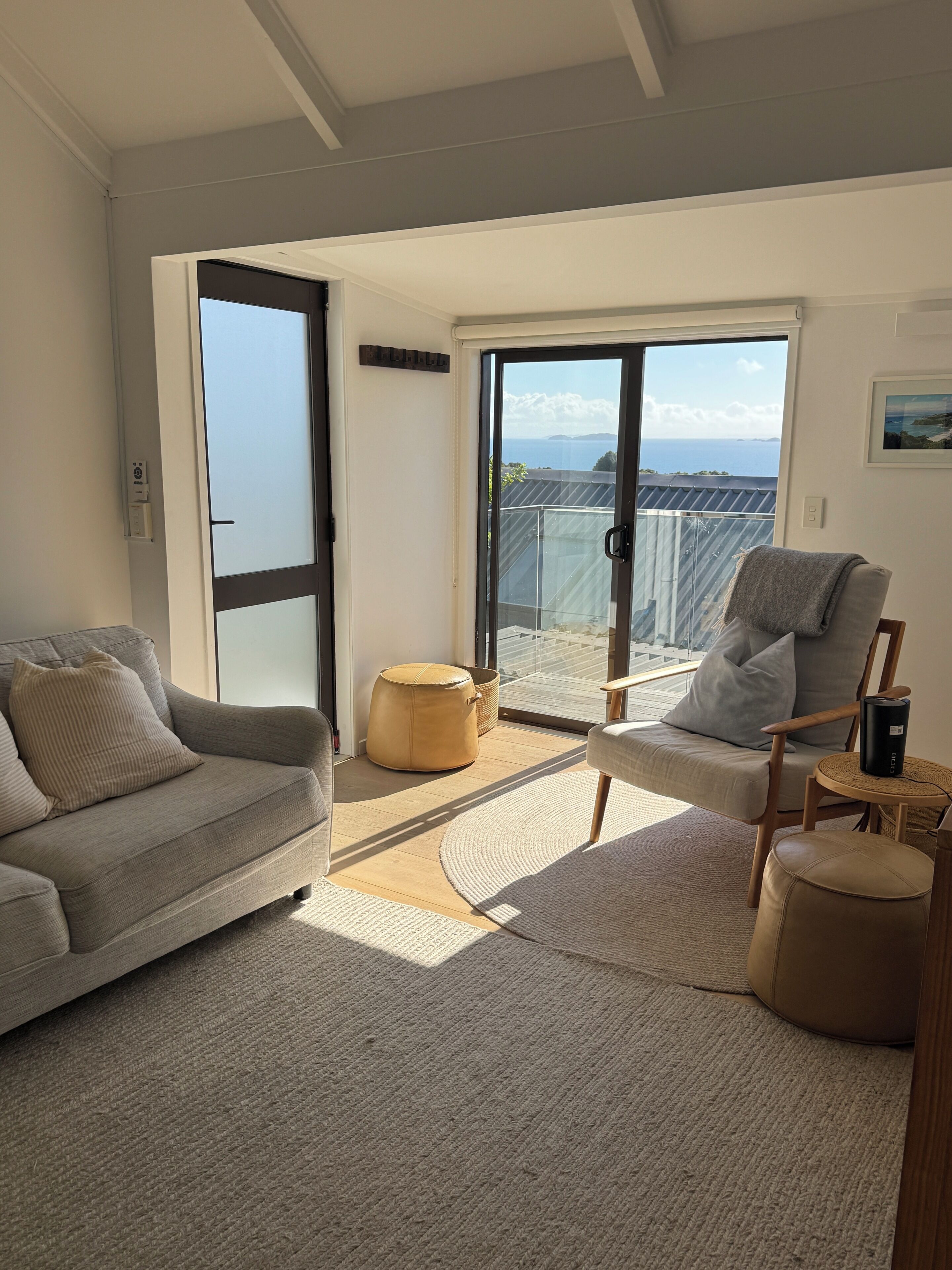 A living room with a sofa, armchair, ottoman, and a view through a sliding door to a balcony.