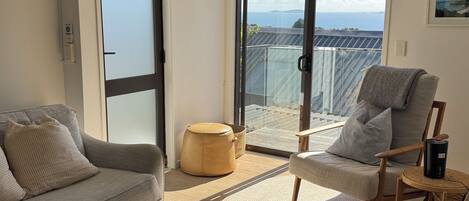 A living room with a sofa, armchair, ottoman, and a view through a sliding door to a balcony.