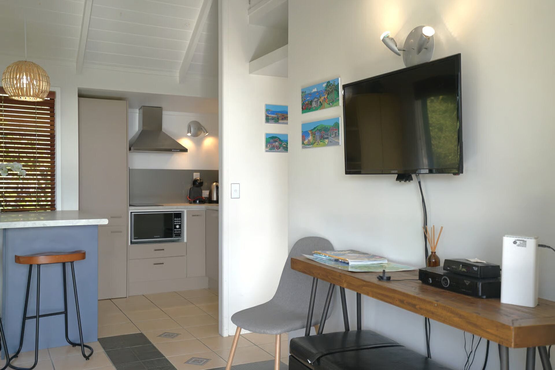A modern kitchen with a microwave, stove, and kettle, a dining area with a table and chairs, and a TV mounted on the wall.
