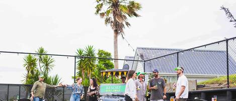 A group of people gathered around a golf cart labeled "RESORT MINI GOLF" in an outdoor setting with tables and chairs, palm trees, and a fence.