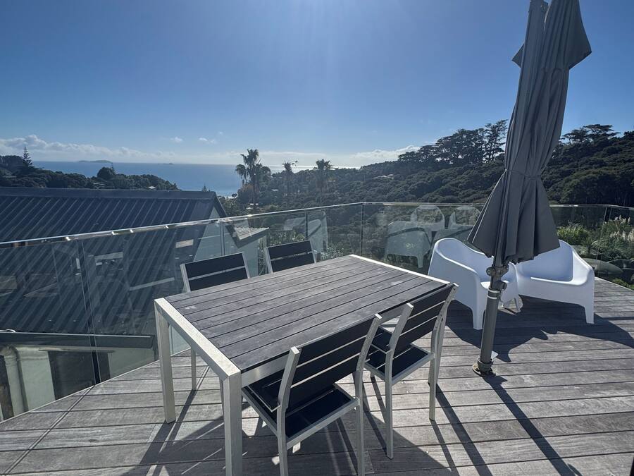 Una terraza con mesa y sillas, una sombrilla y vistas al océano y las colinas.