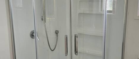 Ein Duschbereich mit Glaswänden, ein weißes Handtuch hängt an der Tür, ein gefliester Boden und eine Toilette auf der rechten Seite.