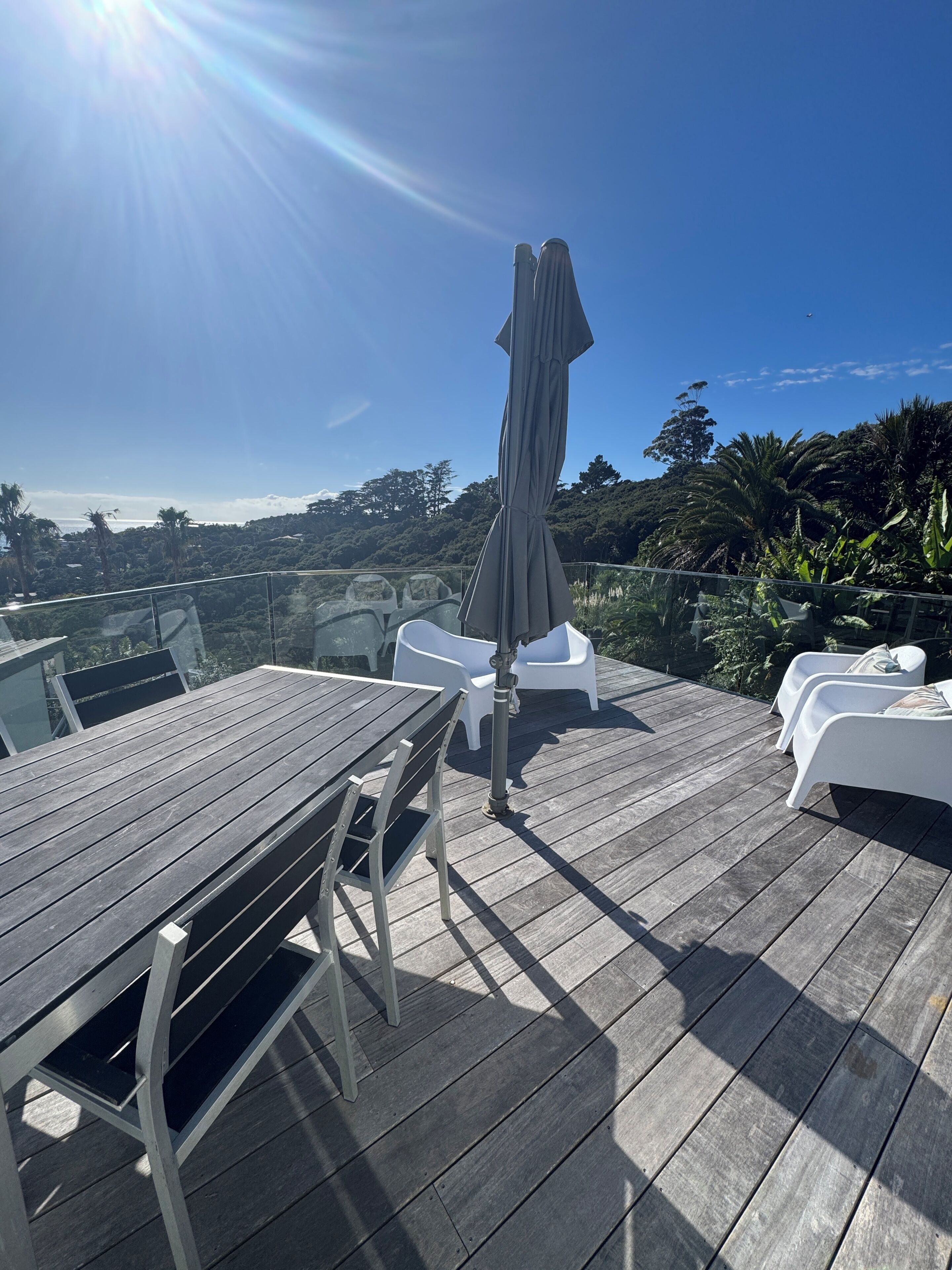 A wooden deck with a table and chairs, an umbrella, and white lounge chairs.