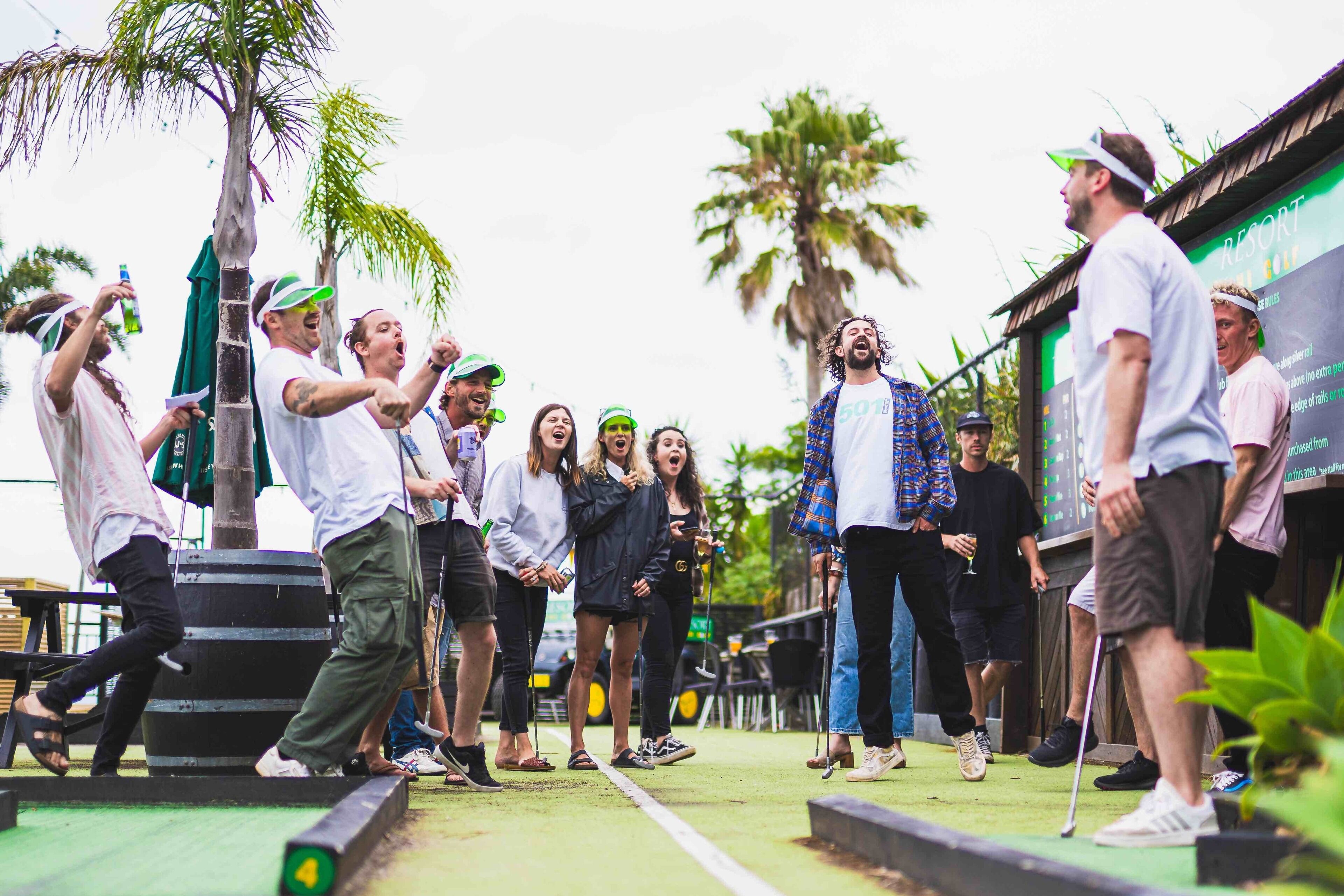 A group of people on a stage with a palm tree and a sign in the background.