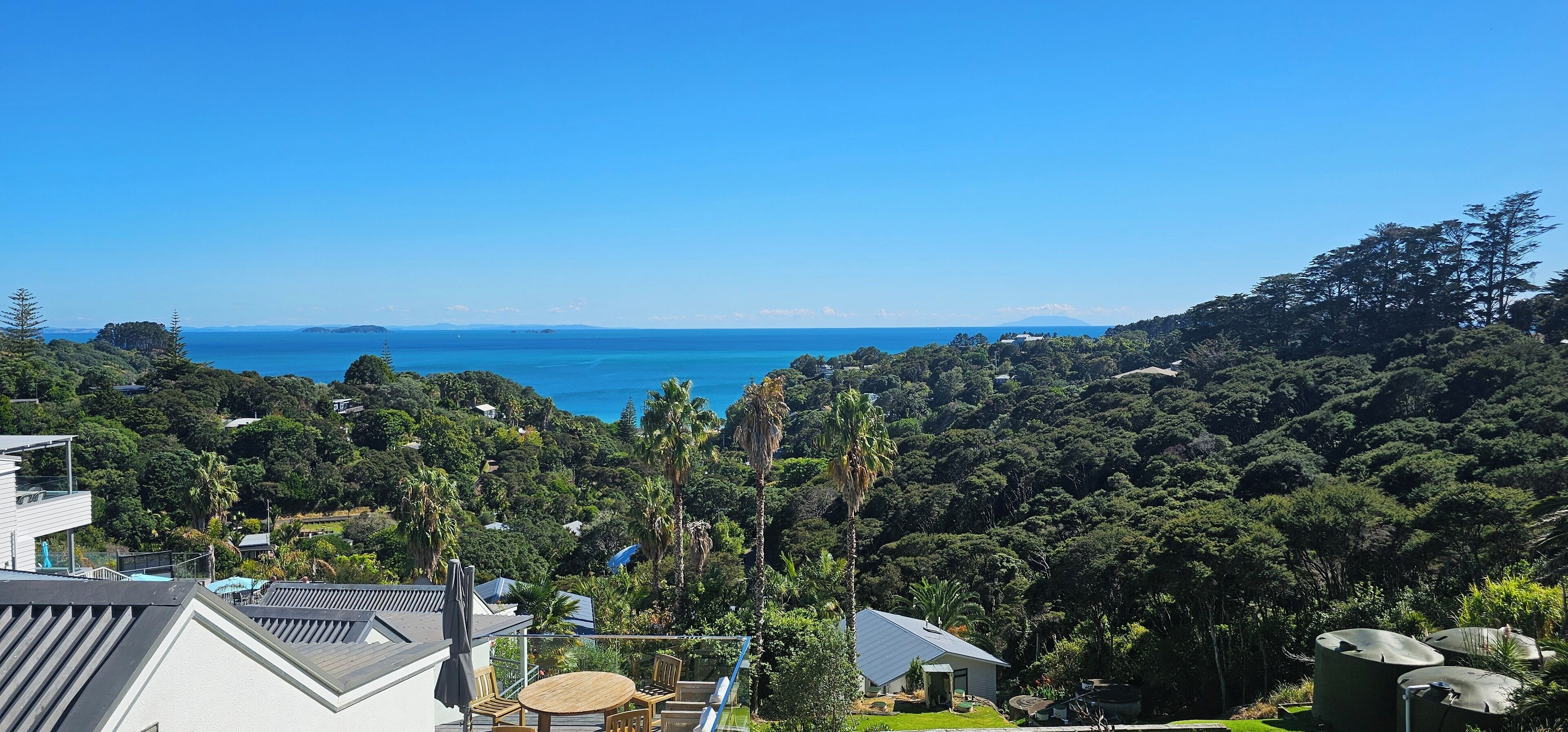 A residential area with a view of the sea, surrounded by dense greenery and houses.