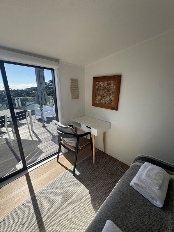 A room with a desk, chair, bed, and a view of the outdoors.