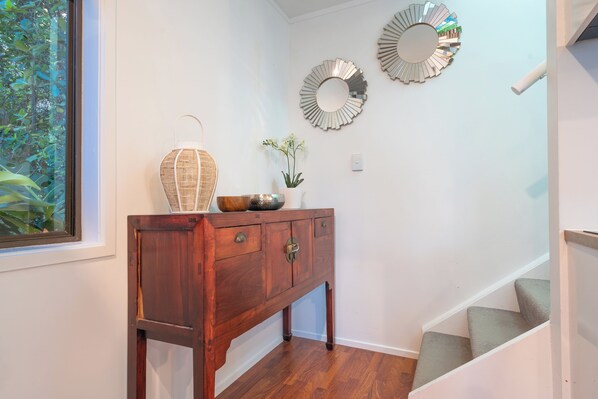 A wooden console table with a vase and a mirror on the wall. - Palm Beach Chalets (Waiheke Island)