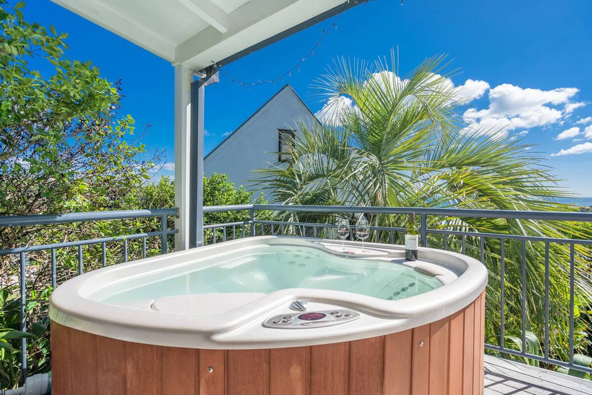 A hot tub on a balcony with a view of a house and palm trees.