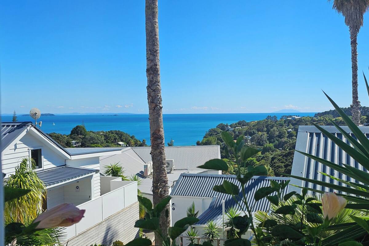A coastal view with a clear sky, palm trees, and modern buildings.