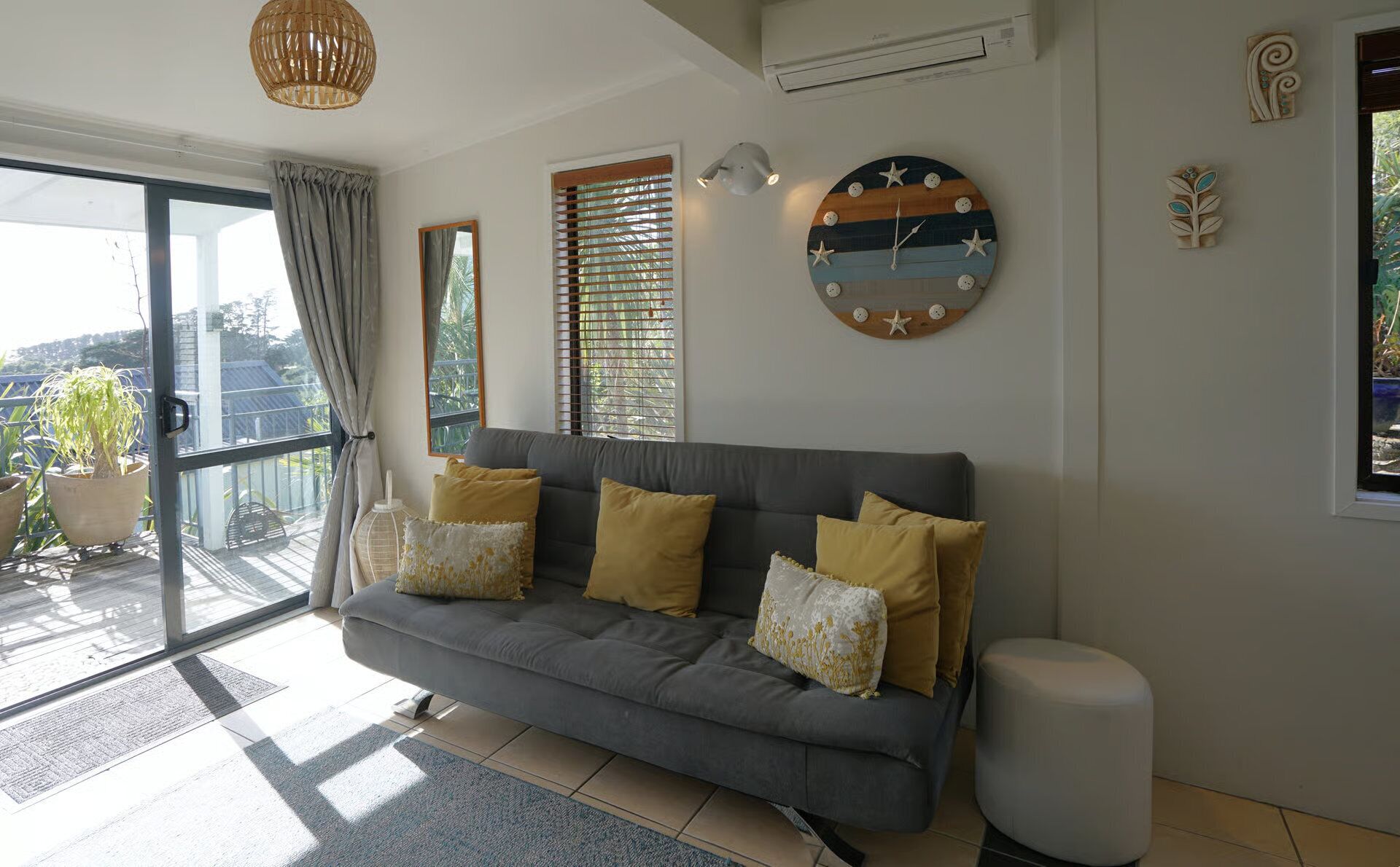 A living room with a grey sofa, a round wall clock, and a potted plant.