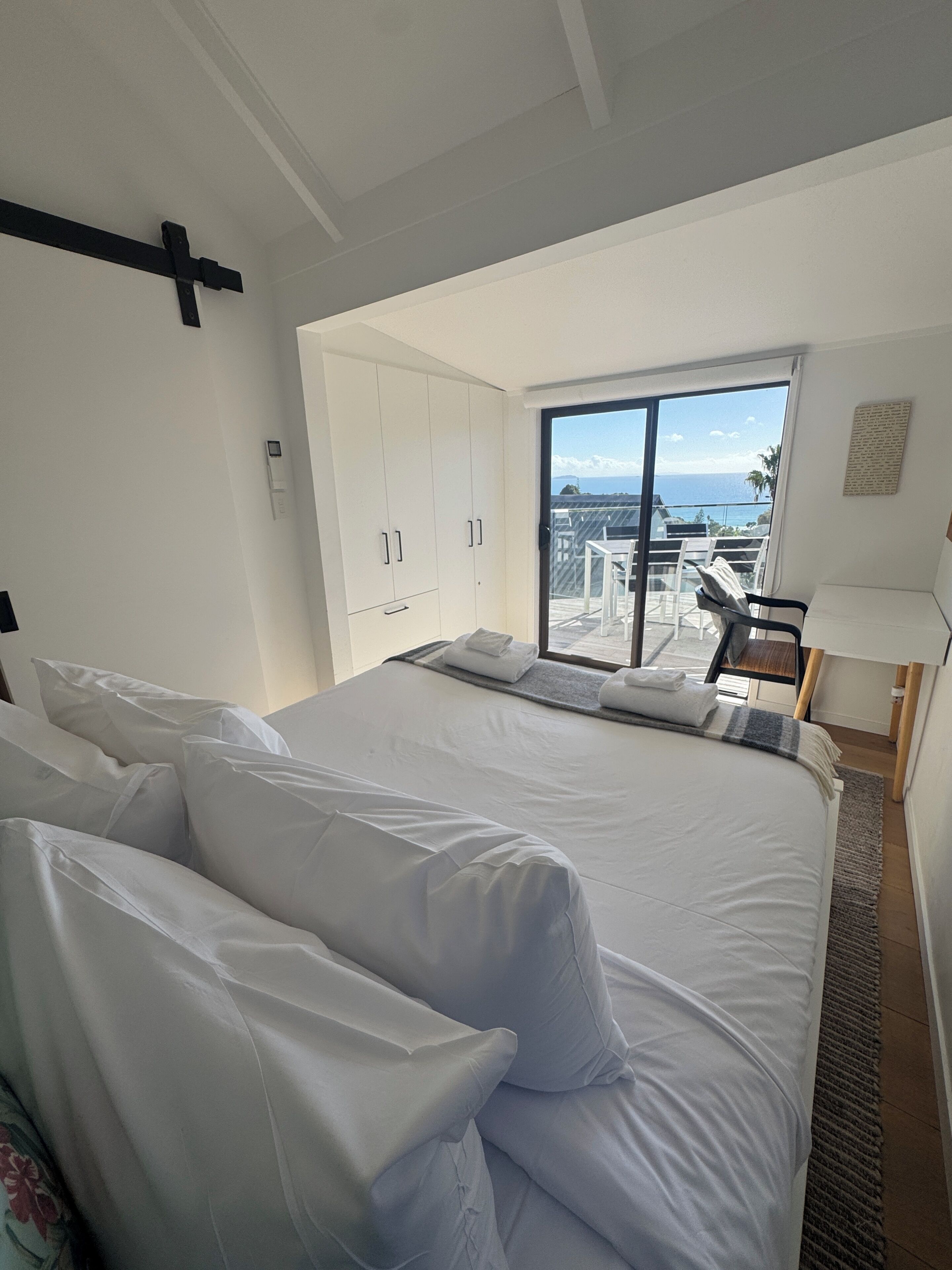 Un dormitorio con una cama grande, un ventanal corredero a un balcón y vista al mar.
