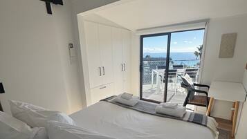 Un dormitorio con una cama grande, un ventanal corredero a un balcón y vista al mar.