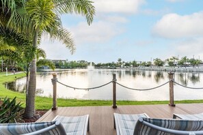 A waterfront deck with lounge chairs, a rope barrier, and a calm lake with a fountain.