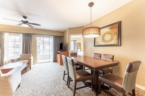 A hotel room with a dining area, a ceiling fan, a television, and a large window.
