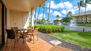 A hotel balcony with wicker furniture, a view of a landscaped area with palm trees, and a fountain.