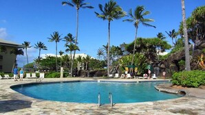 A swimming pool surrounded by palm trees and lounge chairs, with a rocky waterfall feature in the background.