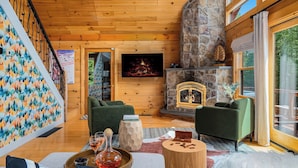 Ein gemütliches Wohnzimmer mit Kamin aus Stein, grünen Sofas und Holzboden.